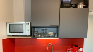 Et lille køkken med indbygget mikroovn, vask med moderne armatur og kaffemaskine.
