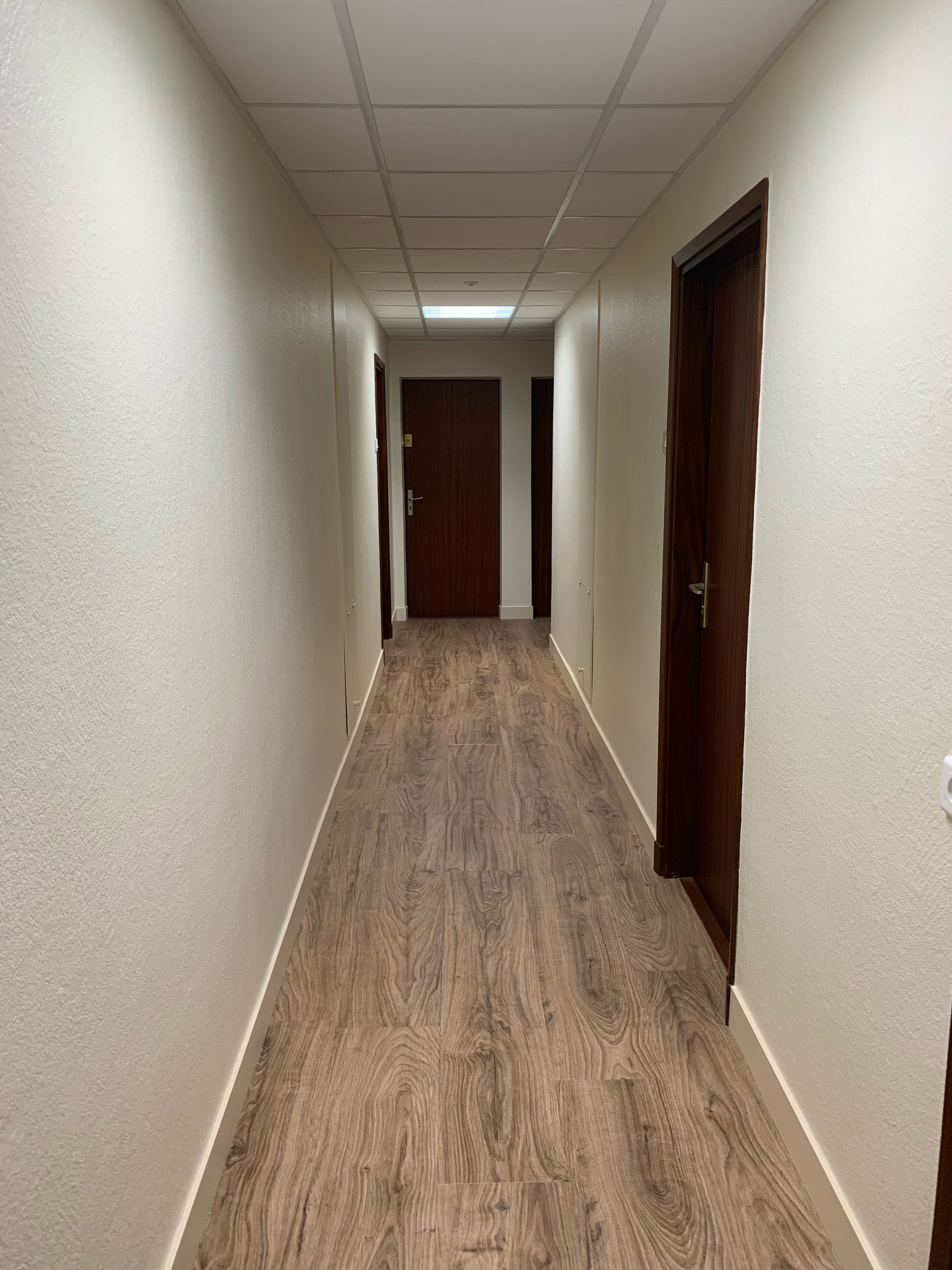 A hallway with wooden flooring and white walls, leading to a door at the end.