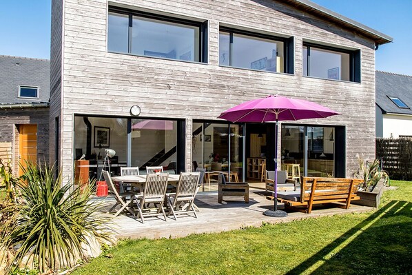 A modern two-story house with a patio area featuring outdoor furniture and a large umbrella.