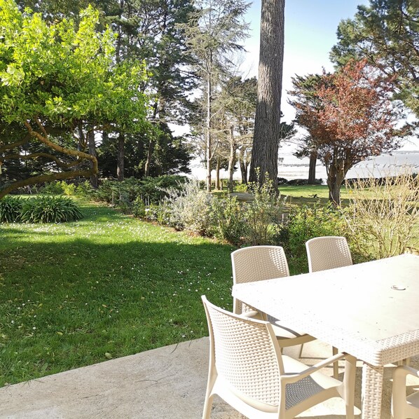 Un patio con mesa y sillas, rodeado de césped y árboles.
