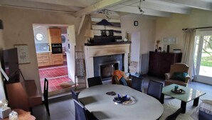 A dining area with a round table, chairs, and a fireplace. There is a kitchen visible in the background. - Nestled in a wooded park, with the beach just 3 minutes away (Pénestin)