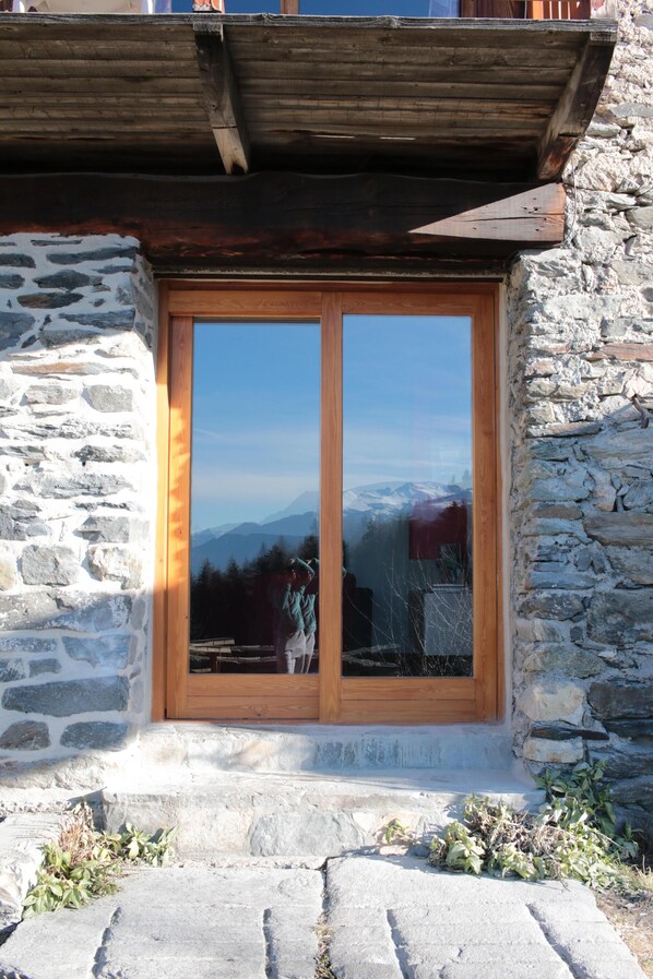 Un edificio de piedra con puerta y ventana de madera, reflejando un paisaje montañoso.
