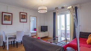 Una sala de estar moderna con un sofá, una mesa de comedor con sillas, un televisor y un balcón con cortinas.