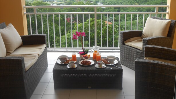 A balcony with wicker furniture, a coffee table with breakfast items, and a scenic view of a green valley. - Villa Standing - Beaches at 400 meters - Swimming Pool (ANSES D'ARLET)
