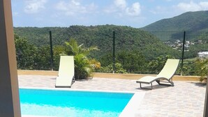 A poolside area with a table and chairs, a view of a mountain and a fence in the background. - Villa Standing - Beaches at 400 meters - Swimming Pool (ANSES D'ARLET)