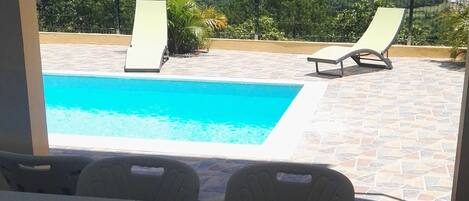 A poolside area with a table and chairs, a view of a mountain and a fence in the background.