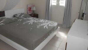 A bedroom with a bed, a nightstand, a lamp, a mirror, and a window with curtains. - Villa Standing - Beaches at 400 meters - Swimming Pool (ANSES D'ARLET)