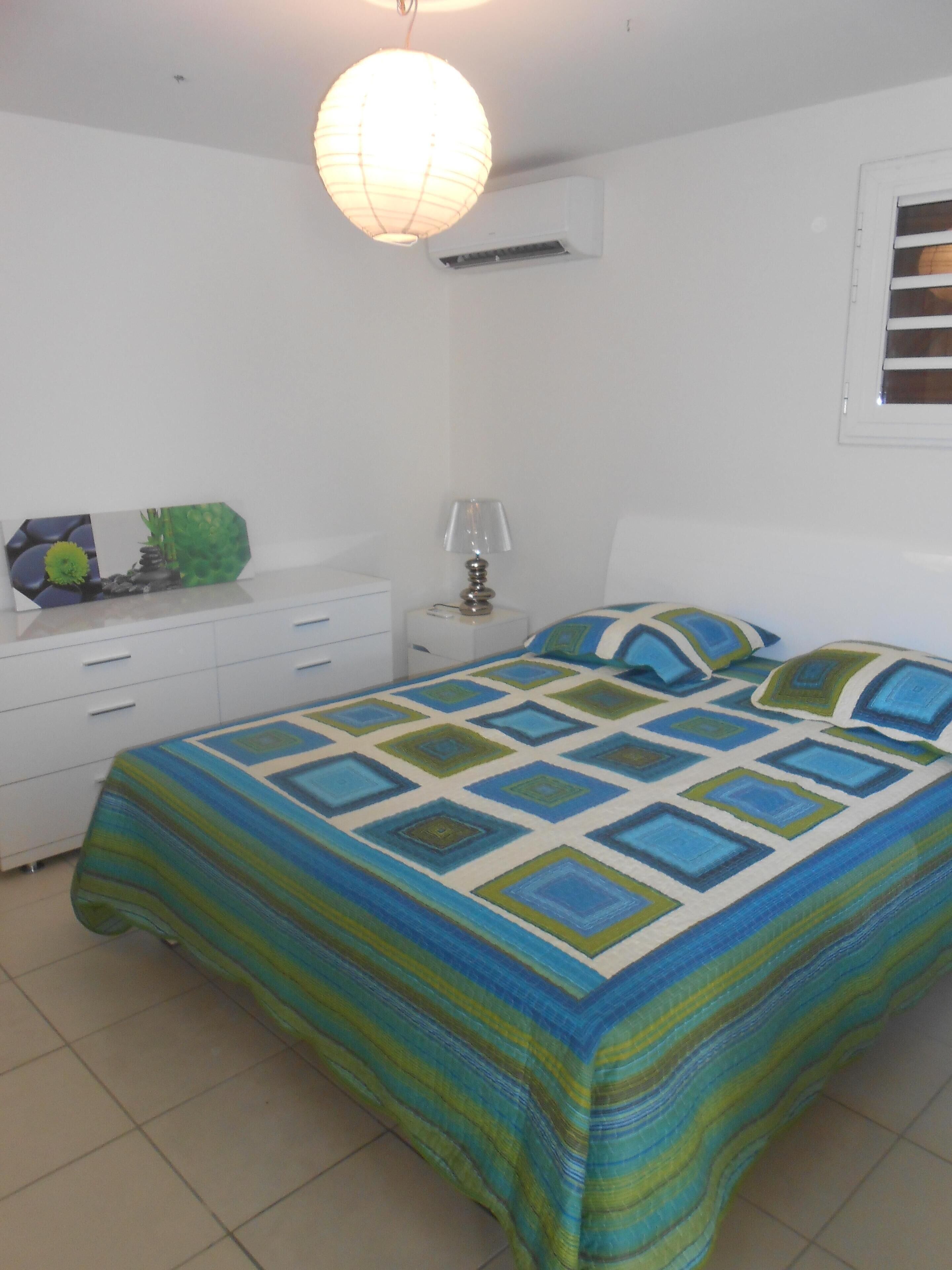 Une chambre à coucher comprenant un lit, une table de chevet, une lampe et un climatiseur fixé au mur.
