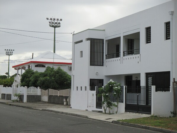 Un bâtiment moderne à deux étages, doté d’une façade blanche, de fenêtres à encadrement noir et d’une entrée sécurisée par un portail.