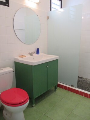 Une salle de bain avec un meuble vert, un lavabo blanc et des toilettes rouges.