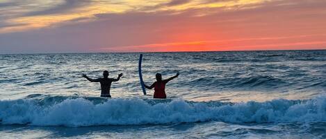 Dos personas en el océano, con los brazos levantados, contemplando la puesta de sol.