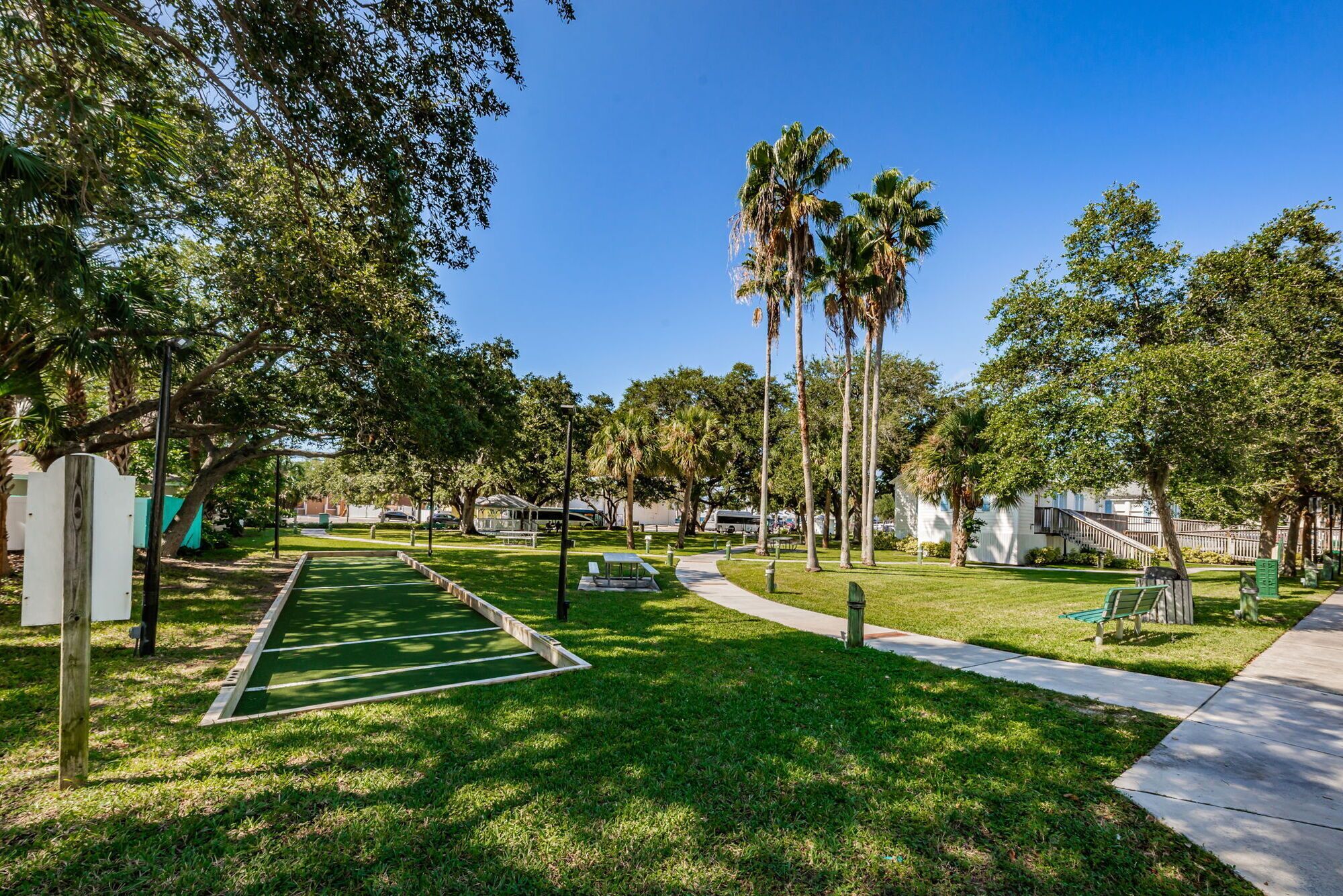 Un parque con césped verde, mesas de picnic y altas palmeras.