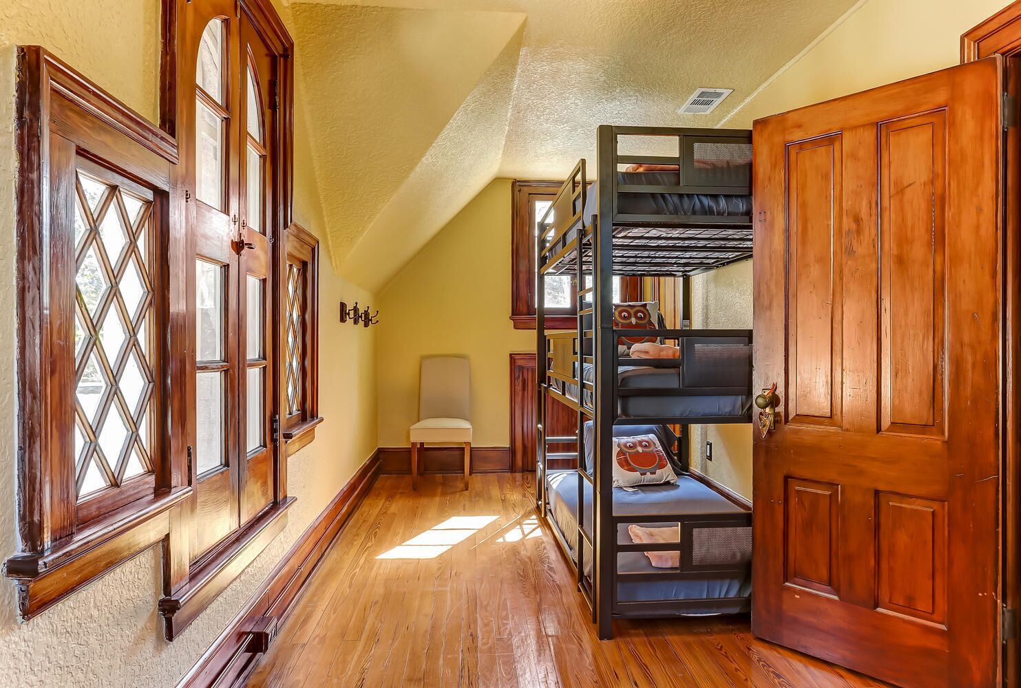 A hallway with wooden floors, a chair, and a bunk bed with owl-themed pillows.