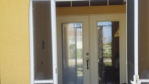 A yellow building with a covered entrance, a sliding glass door, and a small patio area with a doormat.