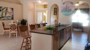 A dining area with a table and chairs, a kitchen with a sink and cabinets, and a painting on the wall.