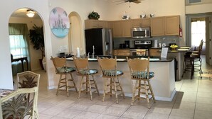 A modern kitchen with wooden cabinets, a central island with bar stools, a ceiling fan, and a dining area with a table and chairs.