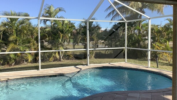 A swimming pool with a clear view of palm trees and a glass enclosure.