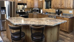 A kitchen with wooden cabinets, granite countertops, stainless steel appliances, and a central island with bar stools.