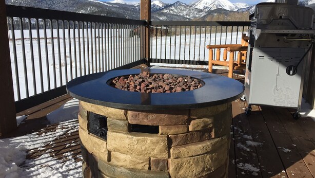 A stone barbecue grill with a black top, set on a wooden deck with snow on the ground.