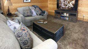 A cozy living room with a grey sofa, patterned cushions, a coffee table, a television, and a bookshelf.