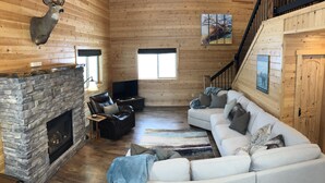 A log cabin interior with a stone fireplace, leather sofa, and a mounted deer head.