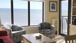 A room with a large window overlooking the sea, two patterned armchairs, a wooden table, and a red sofa. - Beautiful Ocean and Inlet Views From This Newly Updated Corner Unit (North Myrtle Beach)