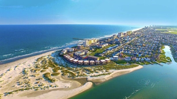 An aerial view of a coastal residential area with beachfront properties, a marina, and a city skyline in the distance. - Beautiful Ocean and Inlet Views From This Newly Updated Corner Unit (North Myrtle Beach)
