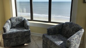 A room with a large window overlooking a beach, two patterned armchairs, and a wall clock. - Beautiful Ocean and Inlet Views From This Newly Updated Corner Unit (North Myrtle Beach)