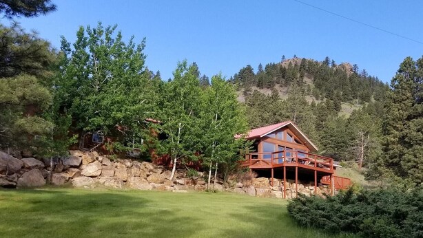 Une cabane avec un toit rouge, une terrasse en bois et un mur en pierre.