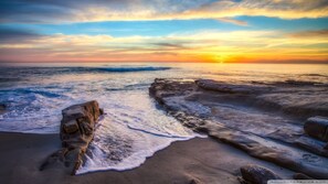 A beach with waves crashing onto the shore, a sunset in the background, and rocky formations. - Beautiful Spacious Beach House Steps Away from the Ocean and Belmont Park (San Diego)