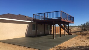 Una casa con un porche cubierto, una terraza de madera y una escalera que lleva a un balcón en el segundo piso.