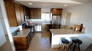 Una cocina con armarios de madera, electrodomésticos de acero inoxidable, una isla central con taburetes y un ventanal que proporciona luz natural.