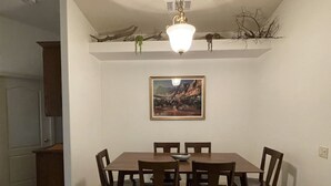 Un comedor con una mesa y sillas de madera, una araña y un cuadro de paisaje en la pared.