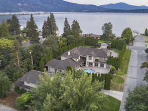 A large house with a swimming pool, surrounded by trees and a lake.