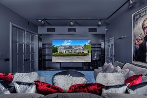 A modern living room with a large flat-screen TV, plush seating, and a framed picture of a house. - Unique Sandpoint Estate, Close to Schweitzer, Covered Spa & Amazing Theater (Sandpoint)