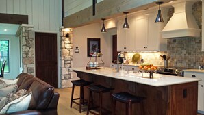 Una cocina moderna con una isla grande, taburetes de bar, un muro decorativo de piedra e iluminación colgante.
