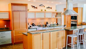 Eine moderne Küche mit Holzschränken, einer zentralen Kochinsel, Edelstahlgeräten und Fischbildern an der Wand.