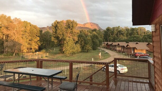 Eine Holzterrasse mit Picknicktischen und Blick auf ein Gebirge mit einem Regenbogen.