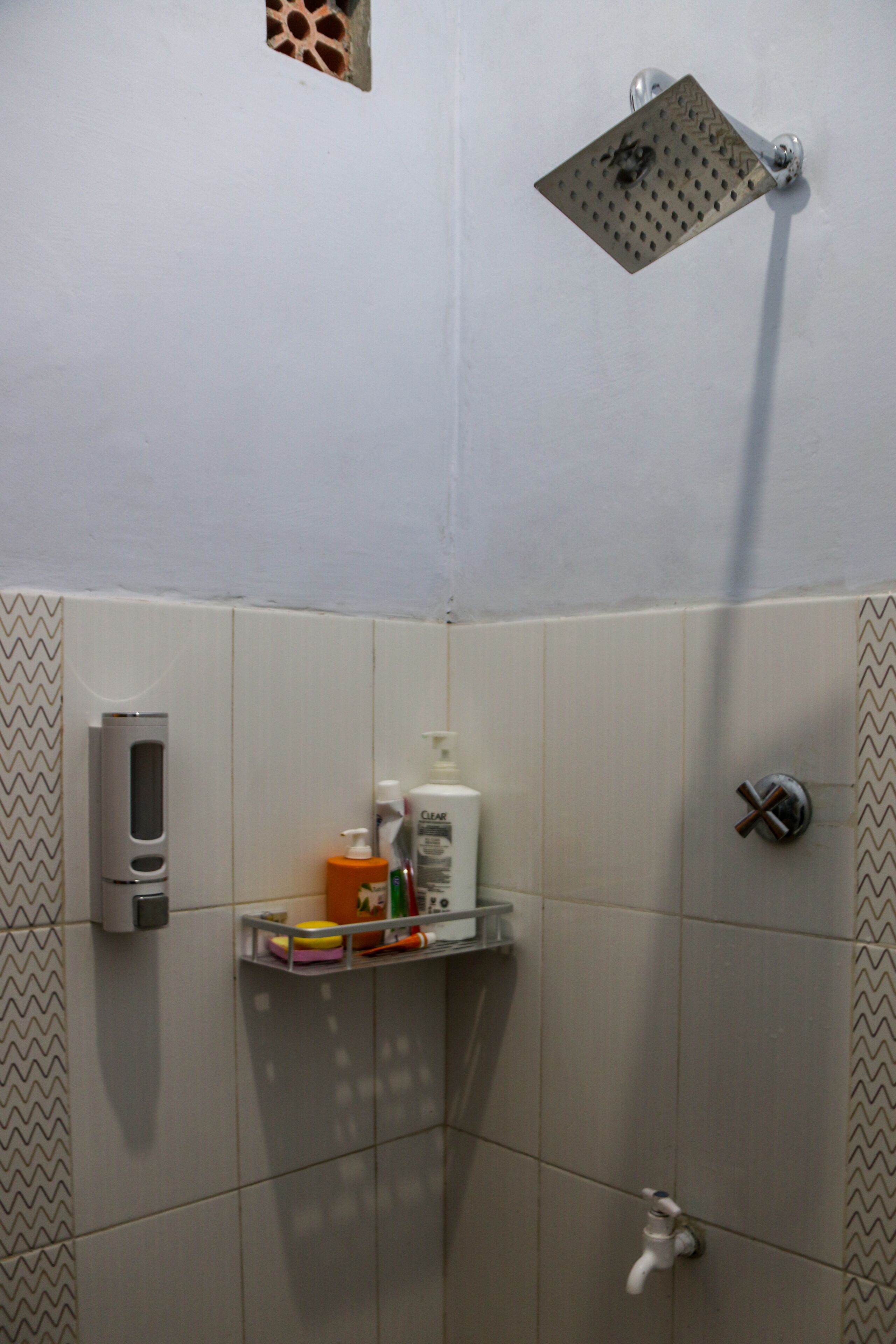Un baño con ducha, dispensador de jabón y un pequeño estante con artículos de aseo.