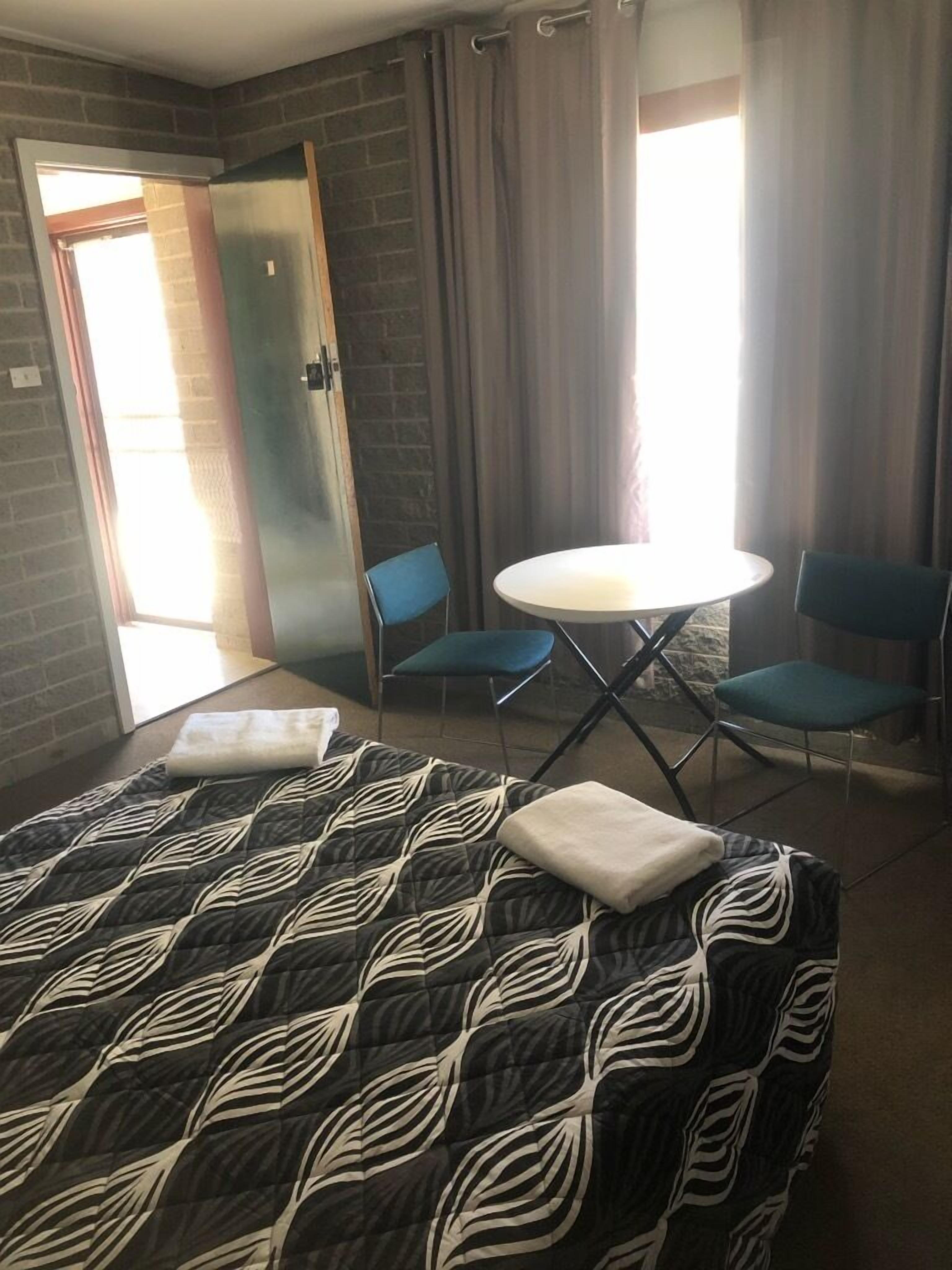 Una habitación de hotel con una cama, dos sillas, una mesita redonda y una puerta que da a un balcón.