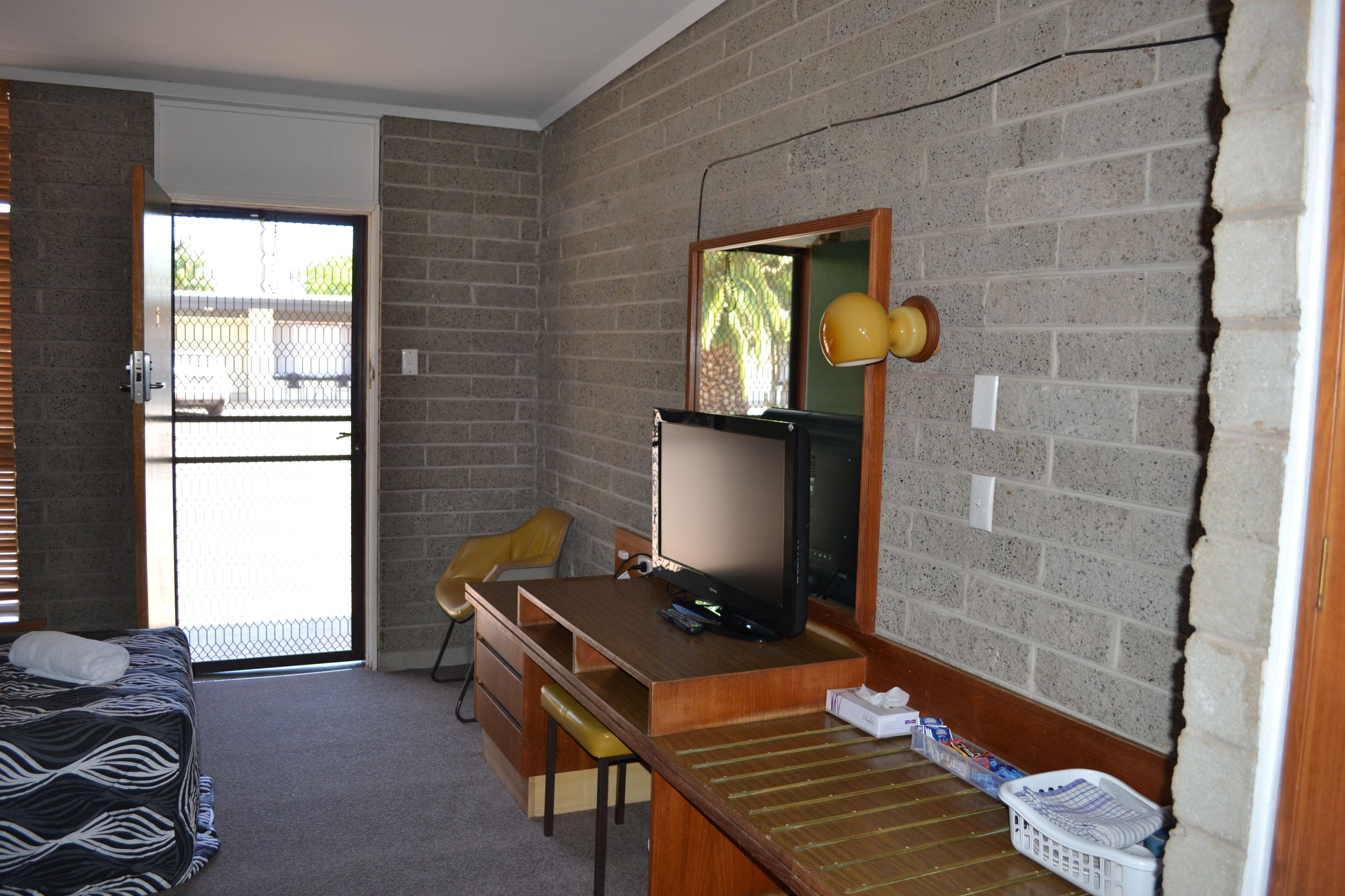 A room with a bed, a desk, a chair, a television, and a window with a view of a fence.