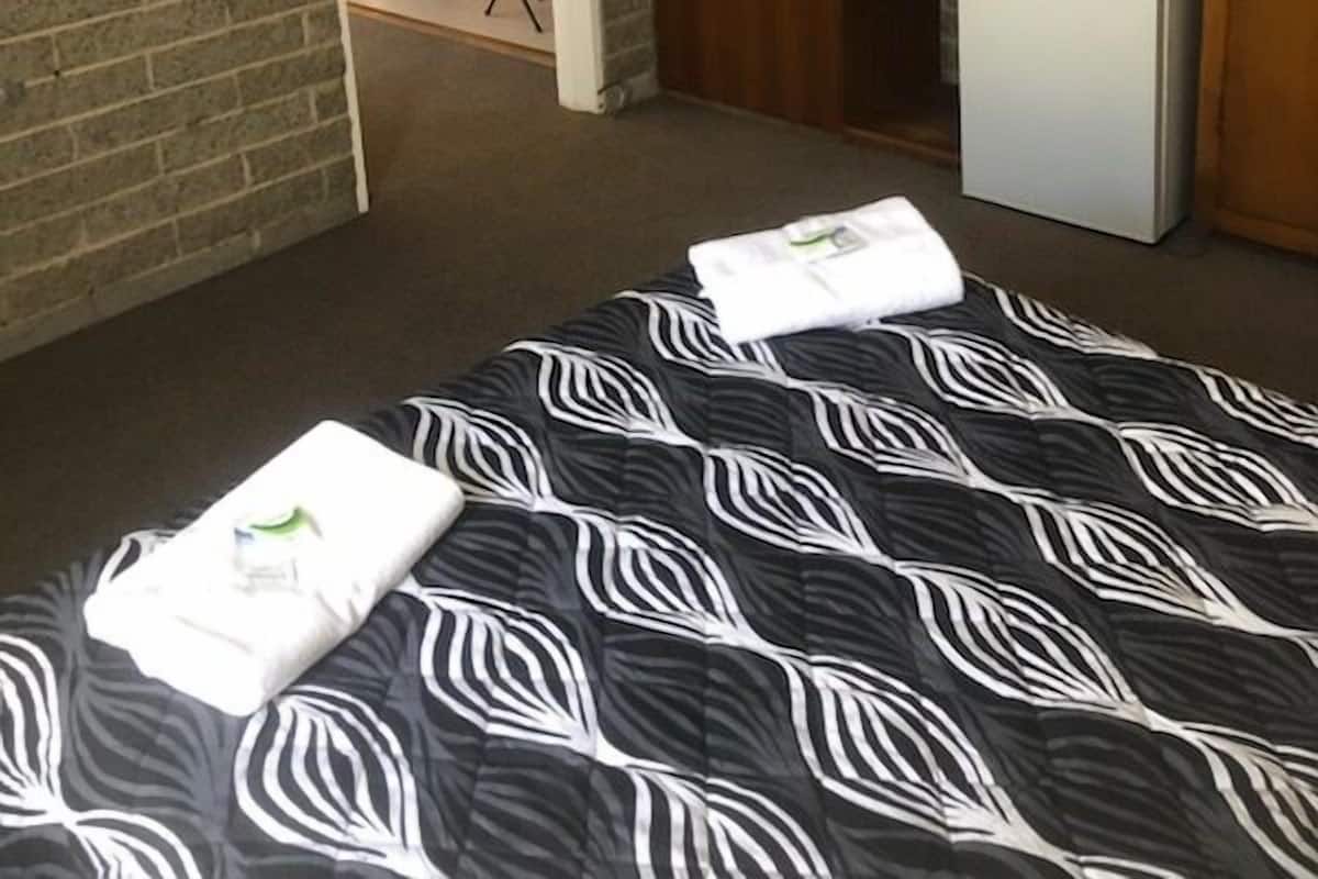 A hotel room with a bed, a small kitchenette, a television, and a brick wall.