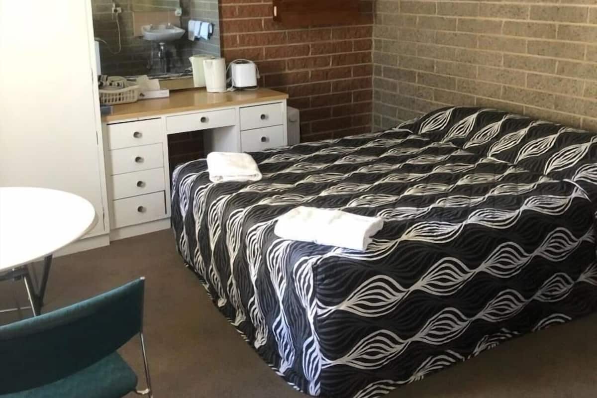 A hotel room with a brick wall, a bed with a patterned bedspread, a desk with a mirror, and a round table.