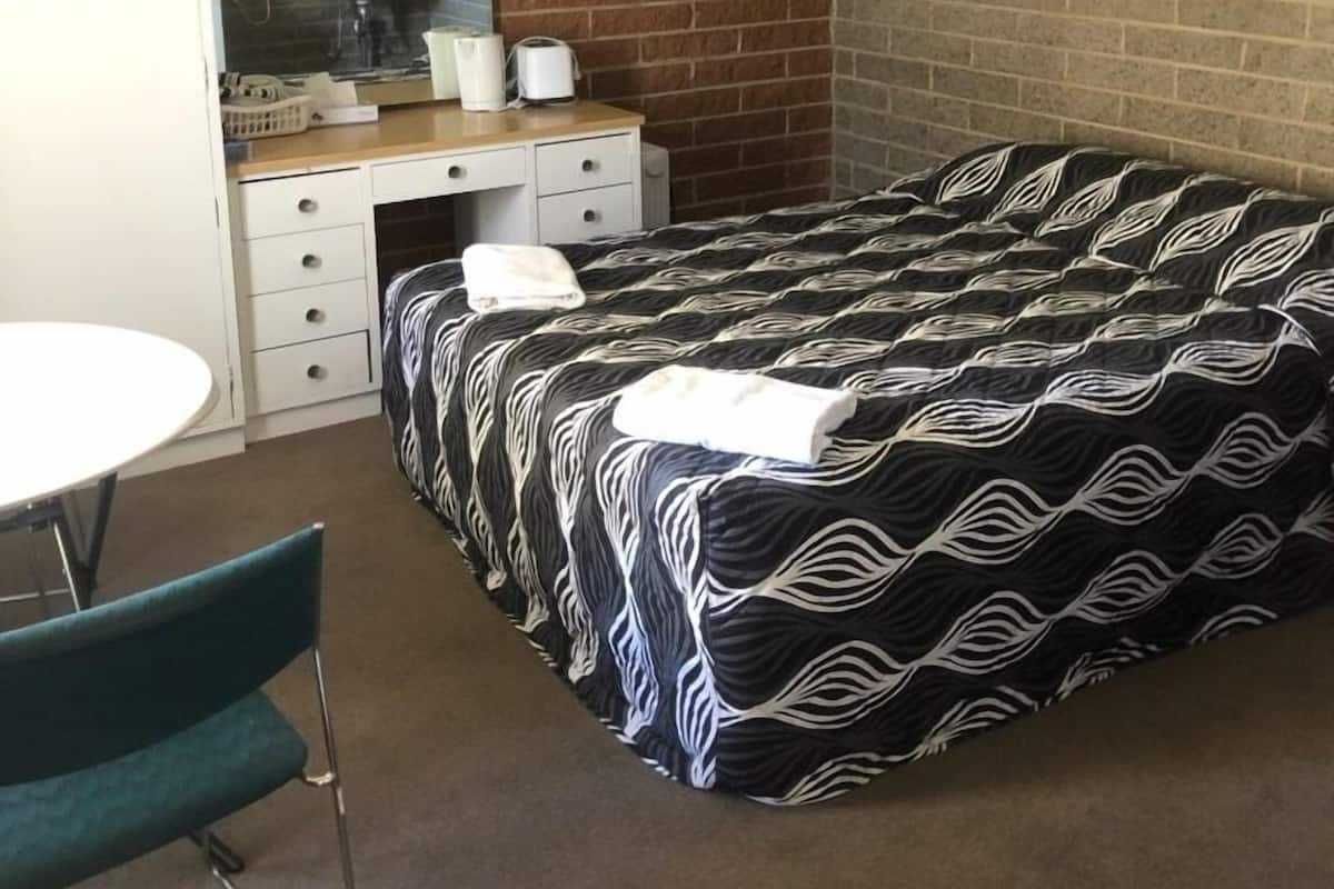 A hotel room with a brick wall, a bed with a patterned bedspread, a desk with a mirror, a sink, and a chair.