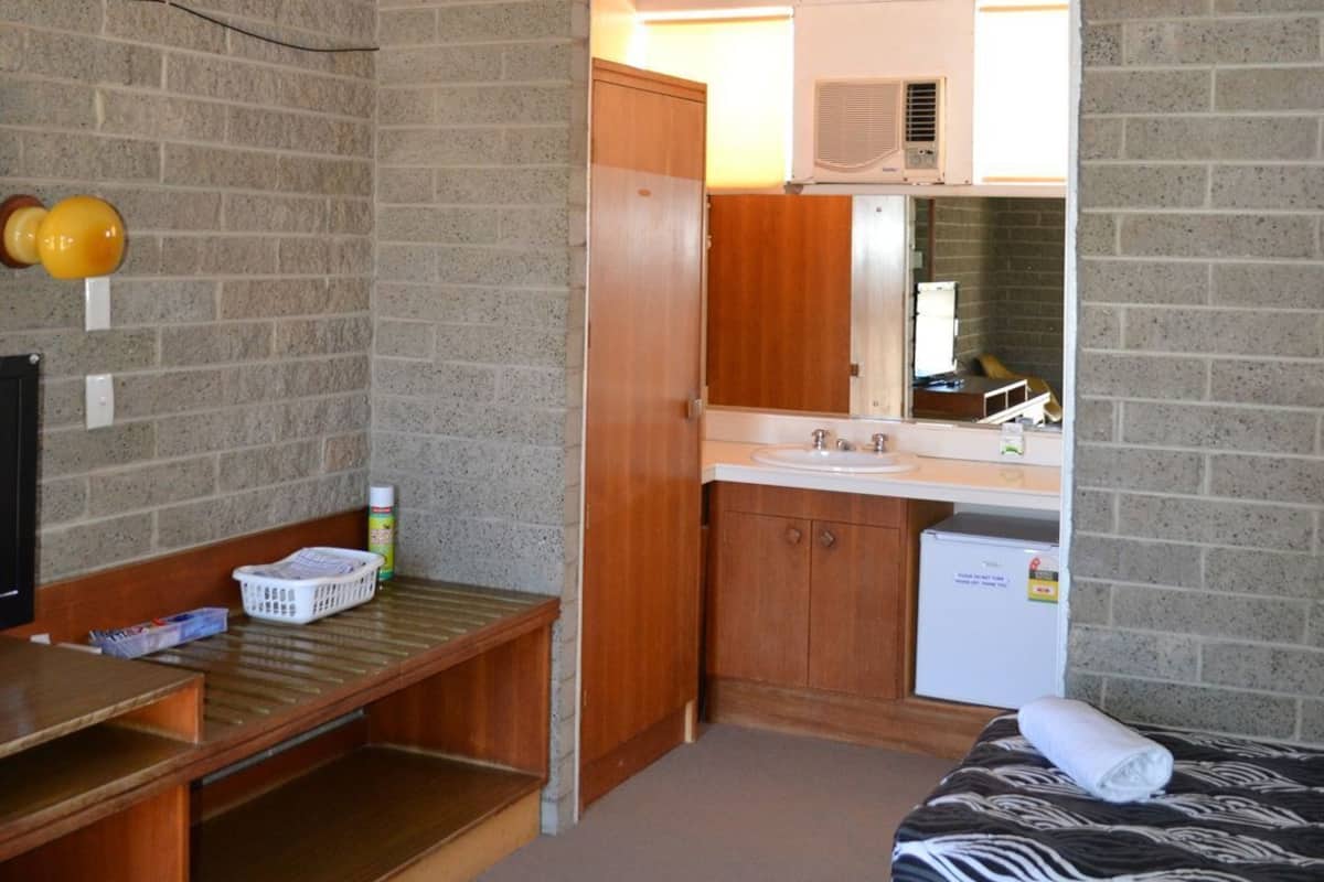 A compact room with a bed, a desk, a small kitchenette, and a brick wall.