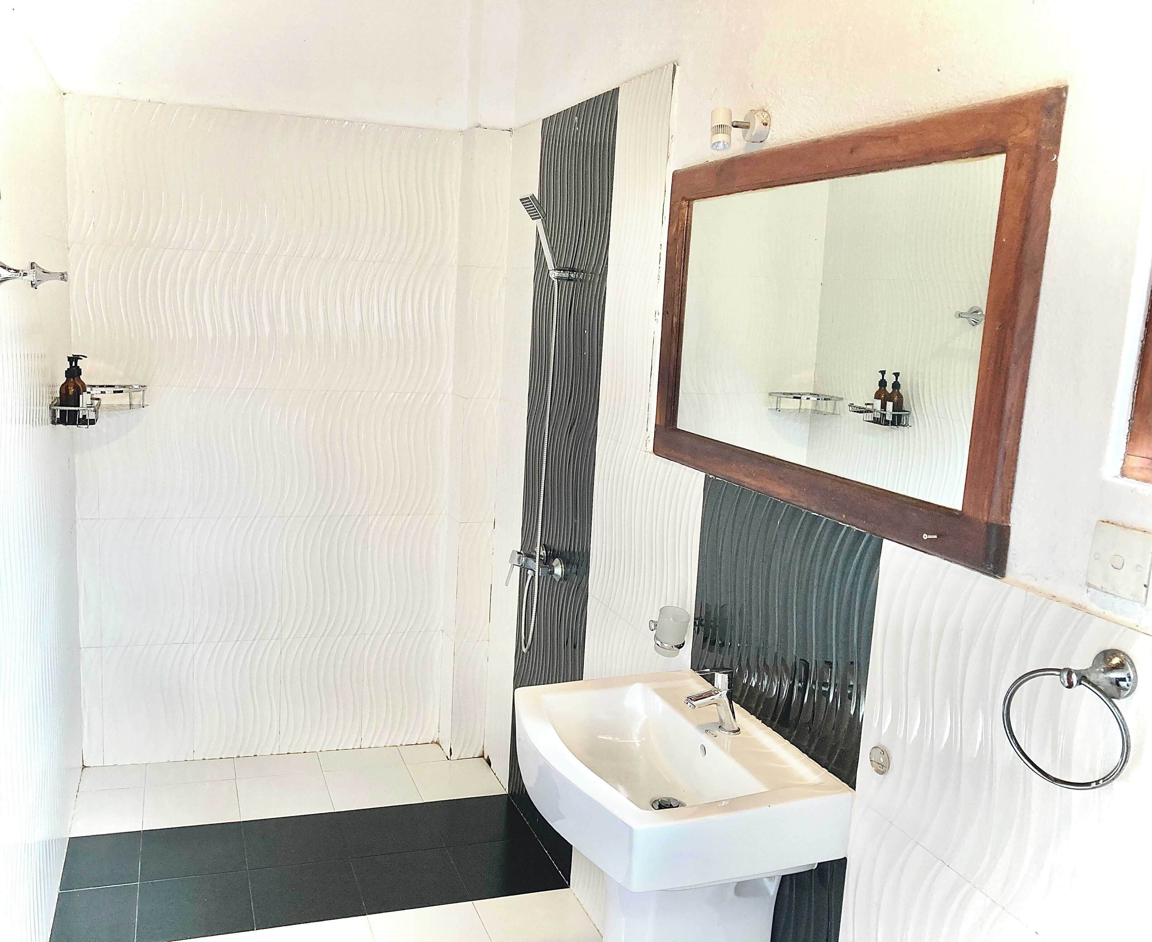 Ein Badezimmer mit einem weißen Waschbecken, einem Spiegel mit Holzrahmen und einer Duschkabine mit gestreifter Vorhang.