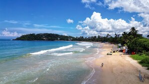 A beach with clear waters, a sandy shore, and a distant forested island. - Seashore Mirissa (Mirissa)