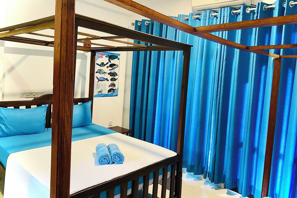 A bedroom with a wooden four-poster bed, a white bedside table, and blue curtains.