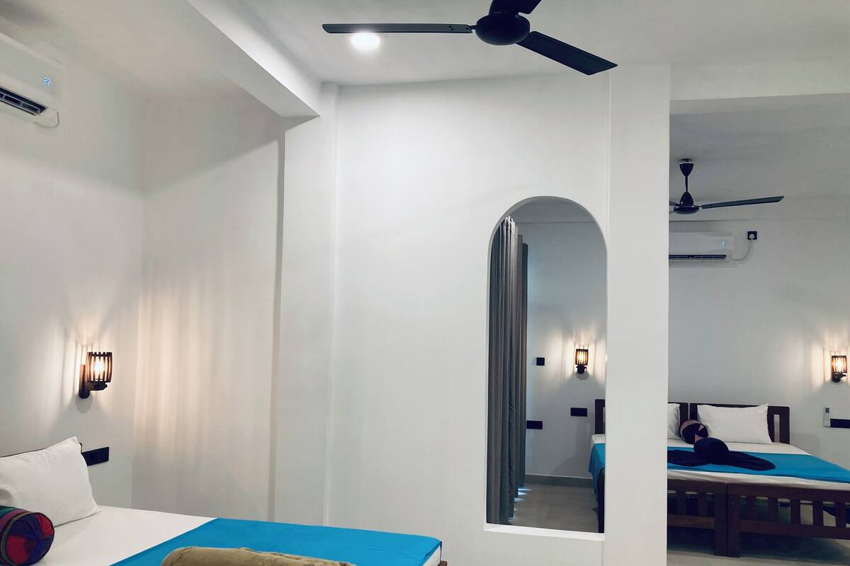 A hotel room with a bed, a ceiling fan, an air conditioning unit, and a mirror.