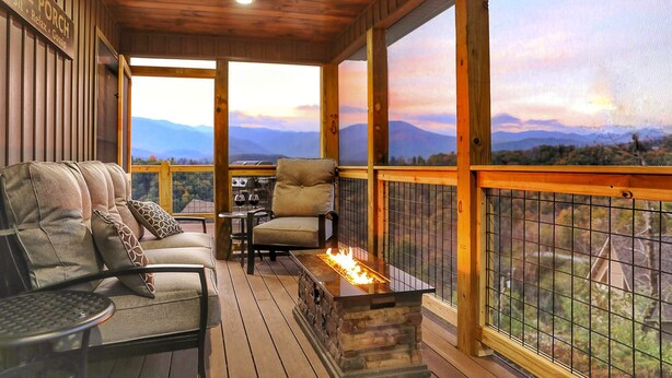 A wooden deck with a stone fire feature, seating, and a view of mountains.